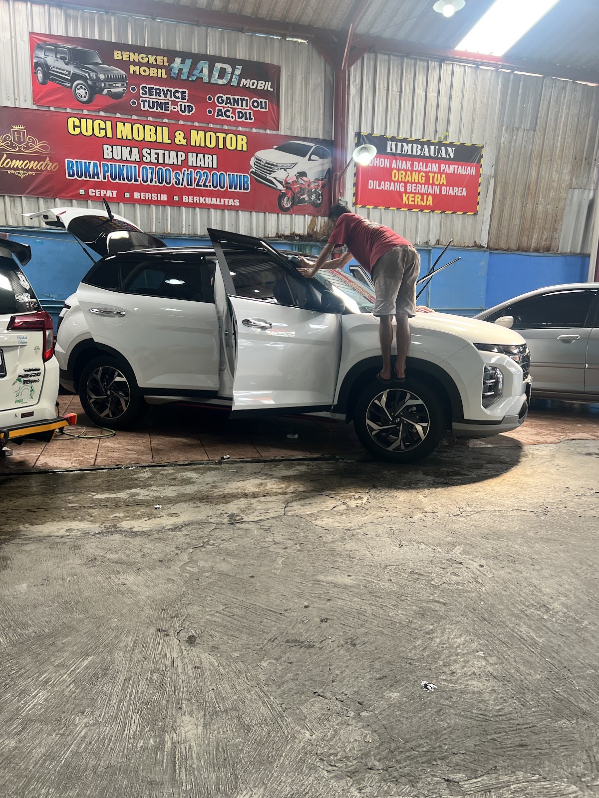 Petugas mengelap bagian atas mobil putih di bay cuci