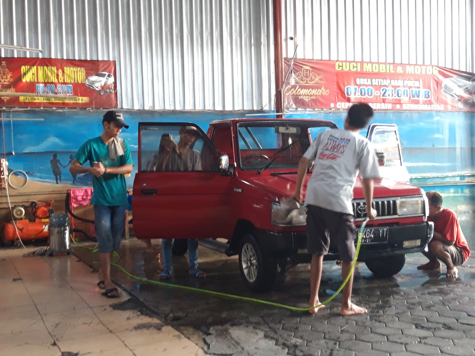 Petugas membersihkan mobil merah dengan pintu terbuka
